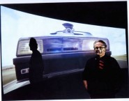 George Miller in front of a projected image of Mad Max's car. 